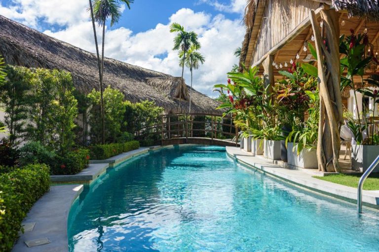 Piscina exterior tropical con puente de madera y cabañas de paja en Takuma Boutik Hotel
