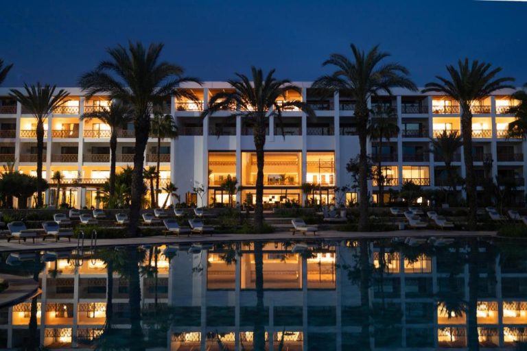 Piscina exterior iluminada de noche con palmeras y tumbonas del hotel The View Agadir