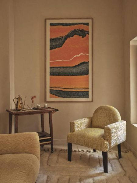 Salón con sillón vintage y obra de arte abstracta en tonos tierra en el hotel IZZA Marrakech