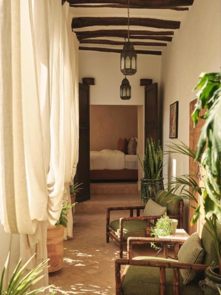 Terraza interior con sillones de bambú y plantas en el Riad IZZA Marrakech con acceso a dormitorio