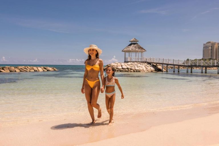 Madre e hija paseando por la playa del Hyatt Ziva Rose Hall All Inclusive con muelle y gazebo al fondo