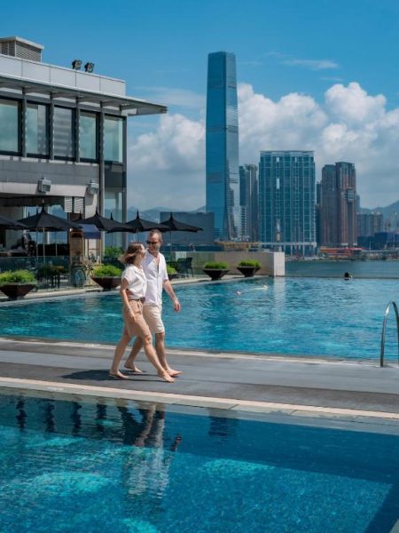 Pareja paseando junto a la piscina infinita del Four Seasons Hotel Hong Kong con vistas al skyline de la ciudad