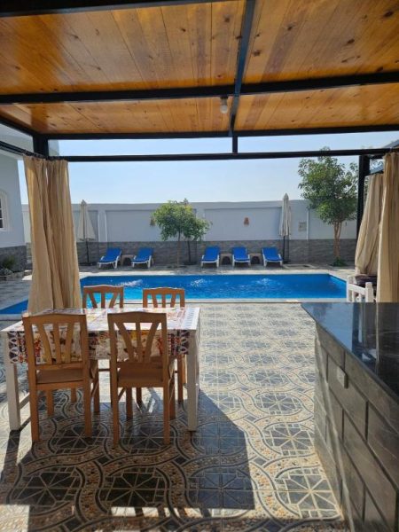 Terraza cubierta con mesa y sillas junto a la piscina exterior del Panorama Hotel con tumbonas azules
