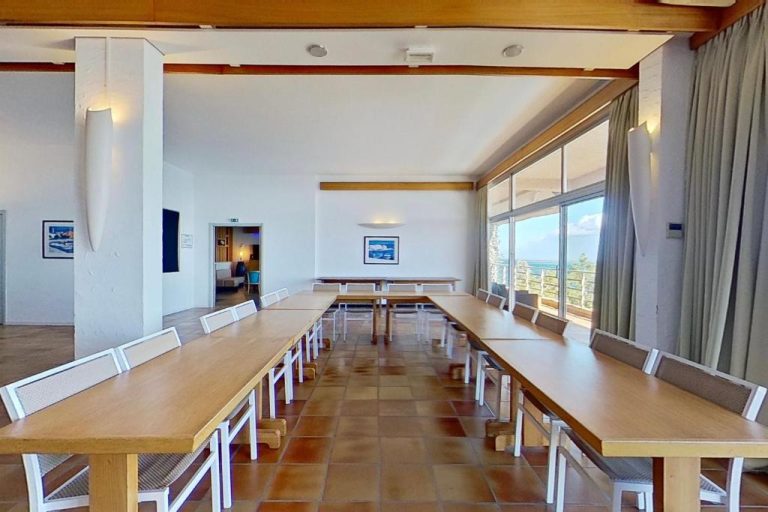 Sala de reuniones con mesas largas y sillas blancas en Hotel Alivi con vistas al mar
