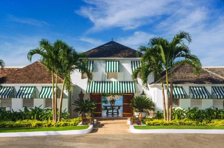 Entrada principal del Round Hill Hotel & Villas con palmeras y toldos verdes en Jamaica