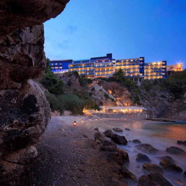Vista nocturna del Hotel Bellevue Dubrovnik iluminado sobre el acantilado con playa privada y faroles