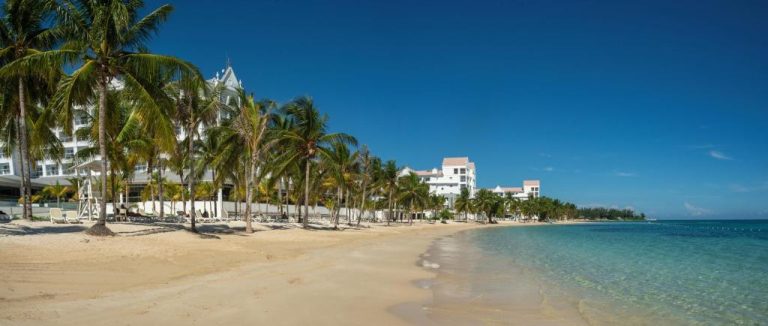 Playa de arena blanca con palmeras y aguas turquesas frente al Hotel Riu Ocho Rios All Inclusive en Jamaica