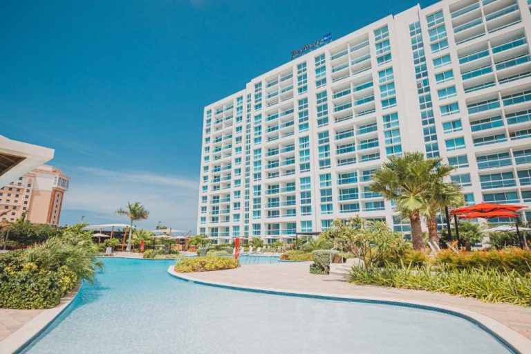 Piscina exterior con jardines tropicales y palmeras del Radisson Blu Aruba bajo cielo azul