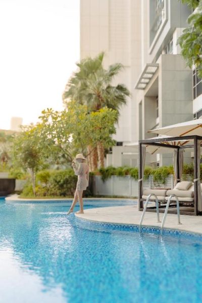 Mujer disfrutando de la piscina exterior con tumbonas y jardines del Taj Dubai hotel de lujo