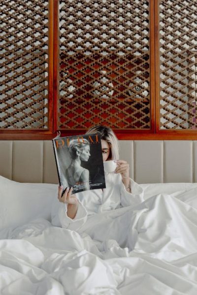 Mujer leyendo revista Dubai y tomando café en cama del lujoso hotel Taj Dubai