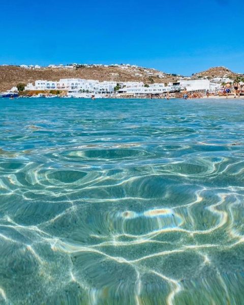 Aguas cristalinas turquesas de la playa frente al Acrogiali Beachfront Hotel Mykonos con vistas a la costa