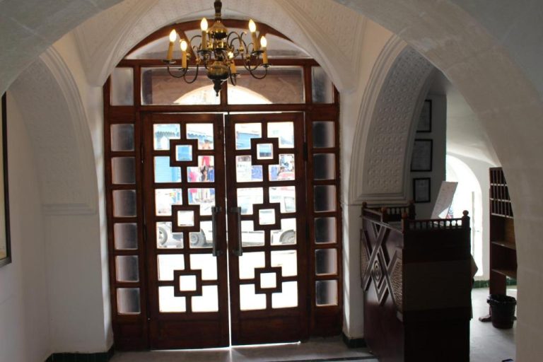 Entrada principal del Hôtel Medina con arcos blancos, puertas de madera y lámpara de araña clásica