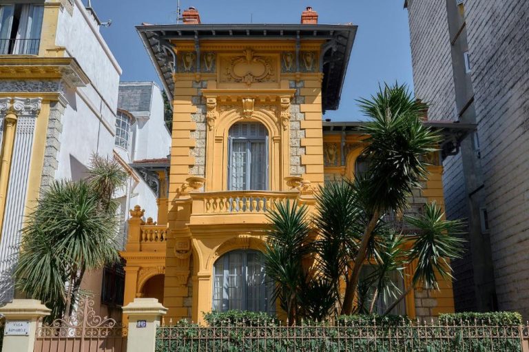 Fachada exterior amarilla de estilo Belle Époque de la Maison des Barons con palmeras y balcón ornamental