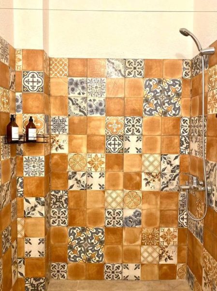 Ducha con azulejos decorativos artesanales en tonos tierra y motivos florales en Casa Rebelión