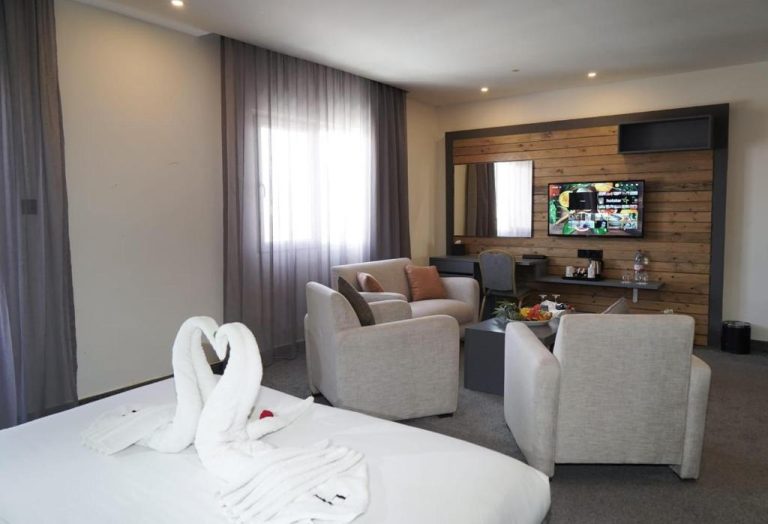 Suite elegante con salón, sofás y TV en pared de madera del Aitch Boutique Hotel LIH