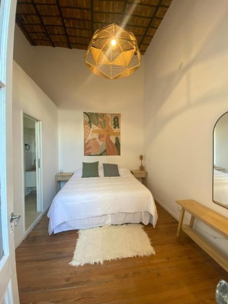 Habitación doble con techo de paja y lámpara artesanal en Casa Rebelión, suelos de madera y decoración natural