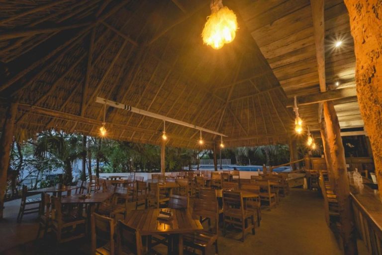 Restaurante palapa del Sotavento Hotel & Yacht Club iluminado de noche con mesas de madera y techo de paja