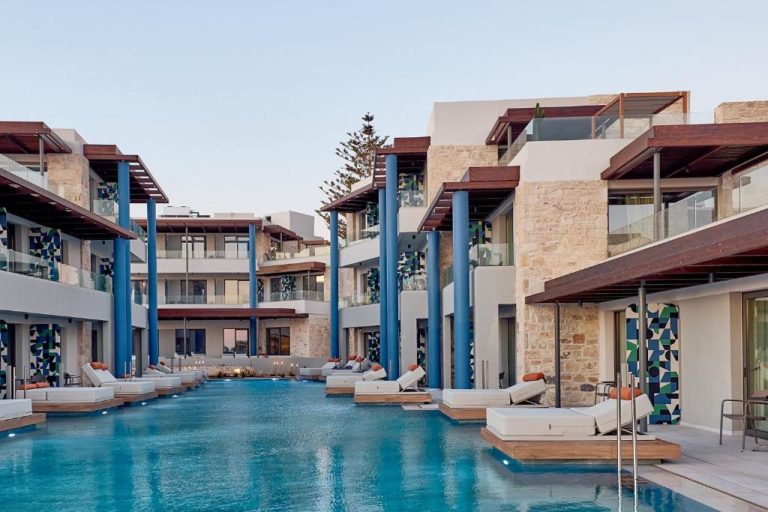 Piscina exterior con tumbonas flotantes y bungalows de lujo en el hotel Paralos Kosta Alímia