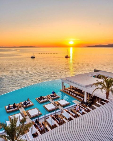 Piscina infinita con tumbonas y vistas al mar al atardecer en el Cavo Tagoo Mykonos