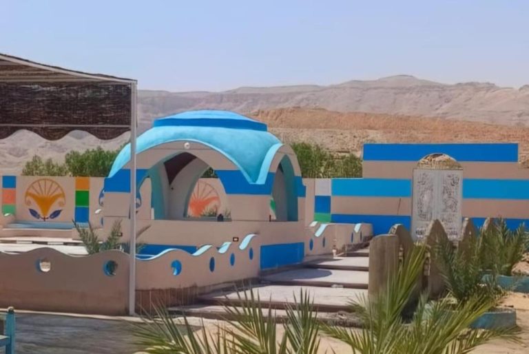 Entrada exterior del Aton Palace Luxor con cúpula azul y murales decorativos rodeada de paisaje desértico