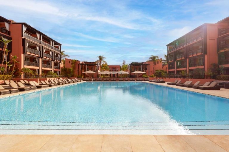 Amplia piscina exterior con tumbonas del Hôtel Barrière Le Naoura rodeada de edificios en Marrakech