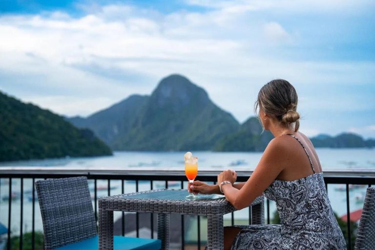 Mujer disfrutando de un cóctel en la terraza del Sea Cocoon Hotel con vistas al mar y montañas de El Nido