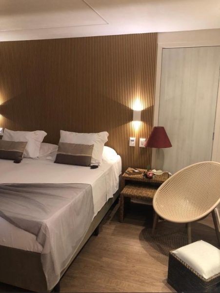 Habitación doble con cama matrimonial, pared de madera y silla ratán en Fortaleza 703-713