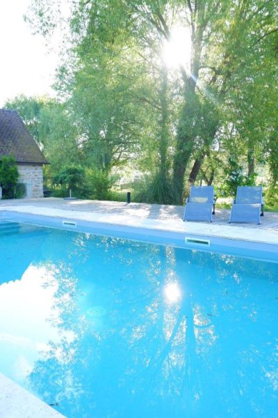 Piscina exterior con tumbonas y jardín frondoso del Moulin de Petoulle en verano