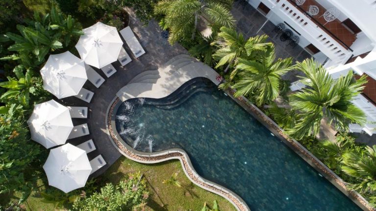 Vista aérea de la piscina exterior con tumbonas y sombrillas blancas del Hotel The Jungle rodeada de vegetación tropical