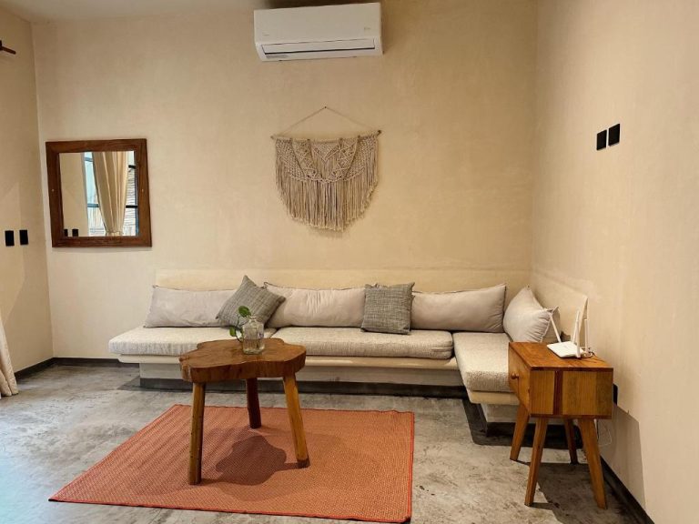 Sala de estar con sofá blanco, mesa de madera y decoración macramé en Casa Kobaab Tulum
