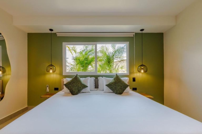 Habitación doble con pared verde y ventana con vistas a palmeras en De la Cruz Studio Apartments