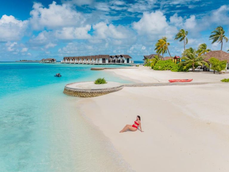 Turista en bikini rojo descansando en la playa de arena blanca del NOOE Maldives Kunaavashi con villas sobre el agua