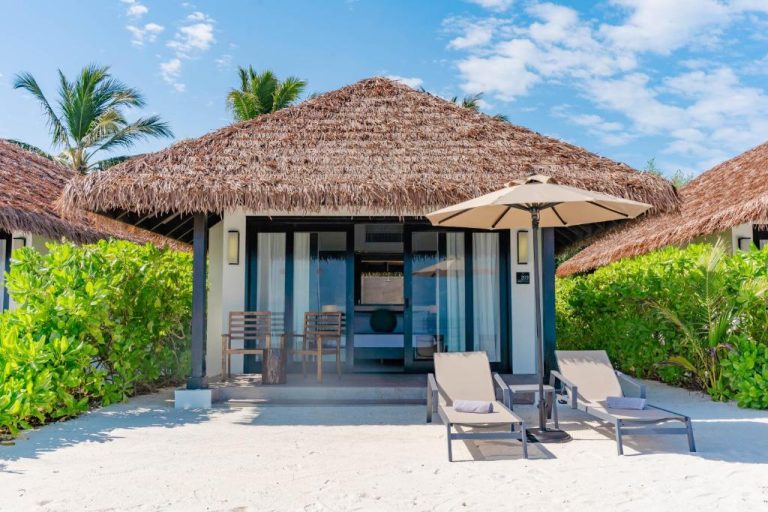Villa de playa con techo de paja y tumbonas en arena blanca del NOOE Maldives Kunaavashi