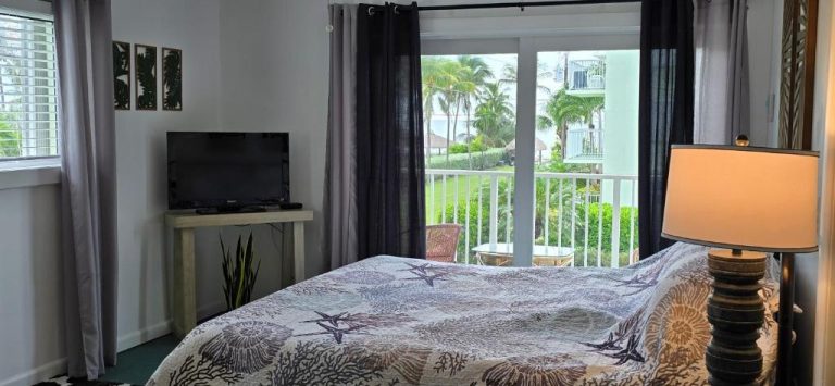Habitación con cama doble, televisión y balcón con vistas a palmeras en Key Colony Beach