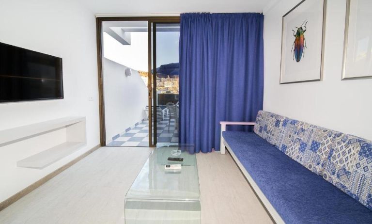 Salón con sofá azul, televisión y acceso a terraza con vistas en Apartamentos Monte Verde