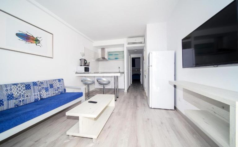 Salón con sofá azul y cocina americana integrada en Apartamentos Monte Verde