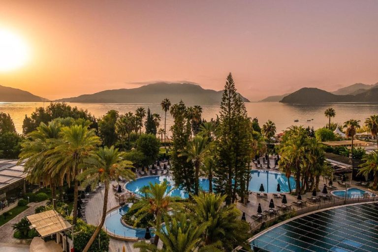 Piscina exterior rodeada de palmeras con vistas al mar y montañas al atardecer en TUI BLUE Grand Azur