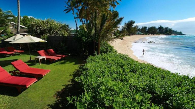 Jardín con tumbonas rojas y sombrillas del Paia Inn frente a la playa de arena en Maui, Hawái