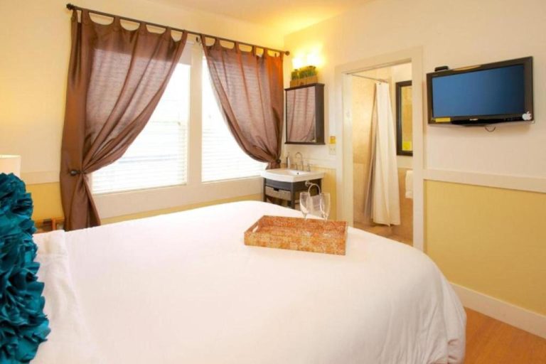 Habitación doble con cama blanca, TV de pared y baño privado en el Paia Inn