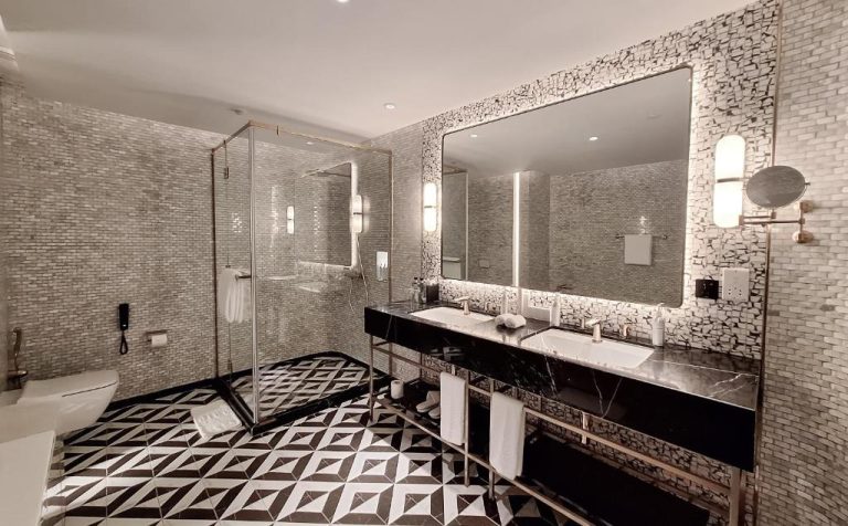 Baño de lujo con doble lavabo de mármol negro y ducha de cristal en Glee Nairobi Hotel
