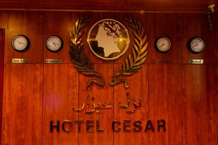 Recepción del Hotel Cesar Palace Sousse con logo dorado y relojes de ciudades del mundo