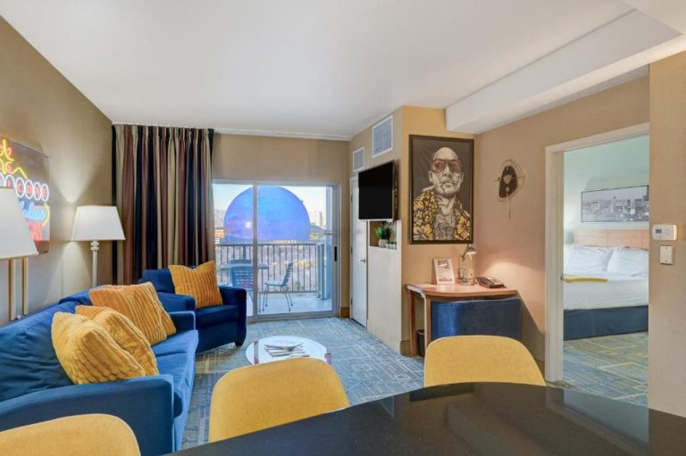 Sala de estar con sofá azul y vistas a la Esfera de Las Vegas desde el balcón en Vintage Vegas Condo