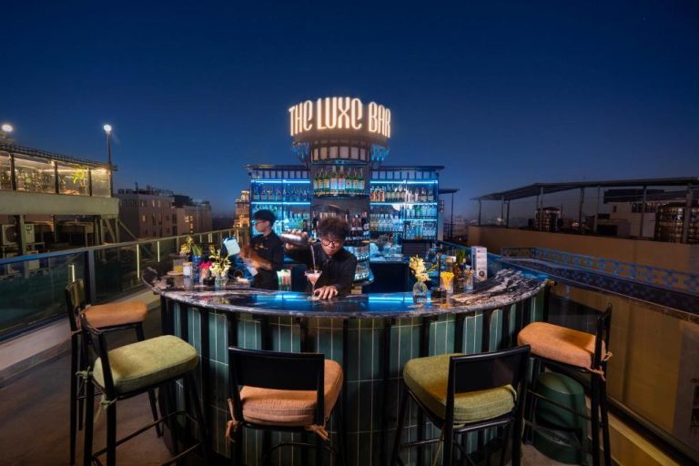 Bar en azotea iluminado de noche en Le Premier Hotel & Rooftop Bar con barmanes preparando cócteles