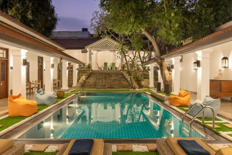 Piscina exterior con tumbonas y puffs de colores en La Maison de Colombo rodeada de jardín