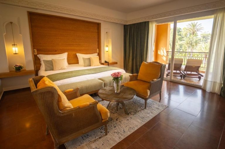 Habitación superior con cama doble, sillones dorados y balcón con vistas a palmeras en Tikida Golf Palace