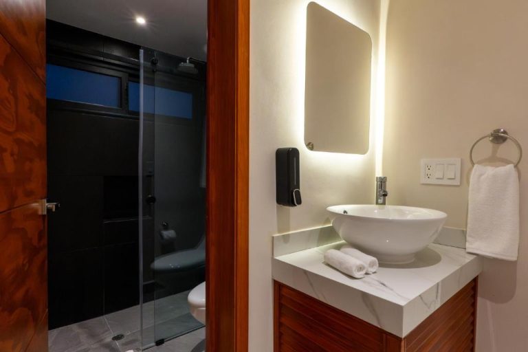 Baño moderno con lavabo redondo, espejo retroiluminado y ducha de cristal en Hotel 28 Cancun