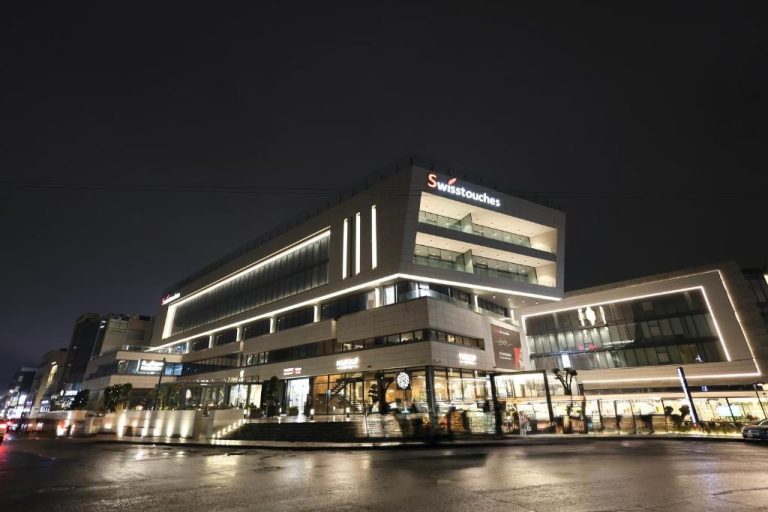 Fachada exterior iluminada de noche del Swisstouches Hotel Amman con restaurantes y zona comercial