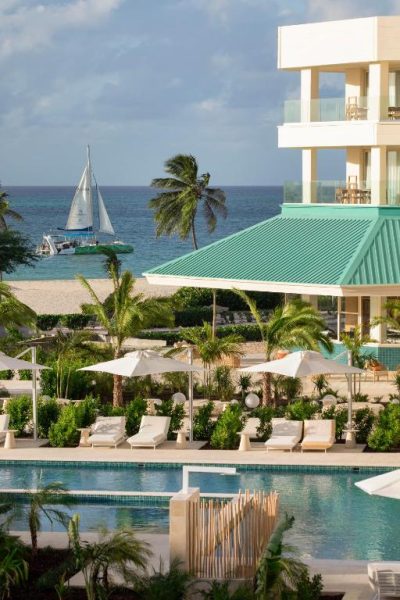 Piscina exterior con tumbonas y vistas al mar del JOIA Aruba by Iberostar con veleros al fondo