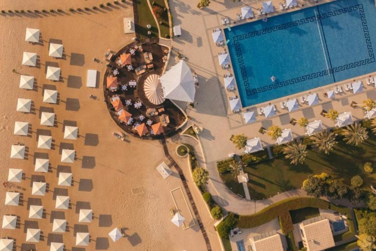 Vista aérea de la piscina exterior y playa privada con sombrillas del The St. Regis Doha