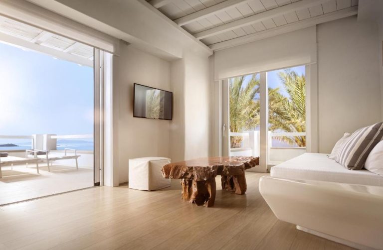 Salón de suite con mesa de madera natural y vistas al mar en Cavo Tagoo Mykonos